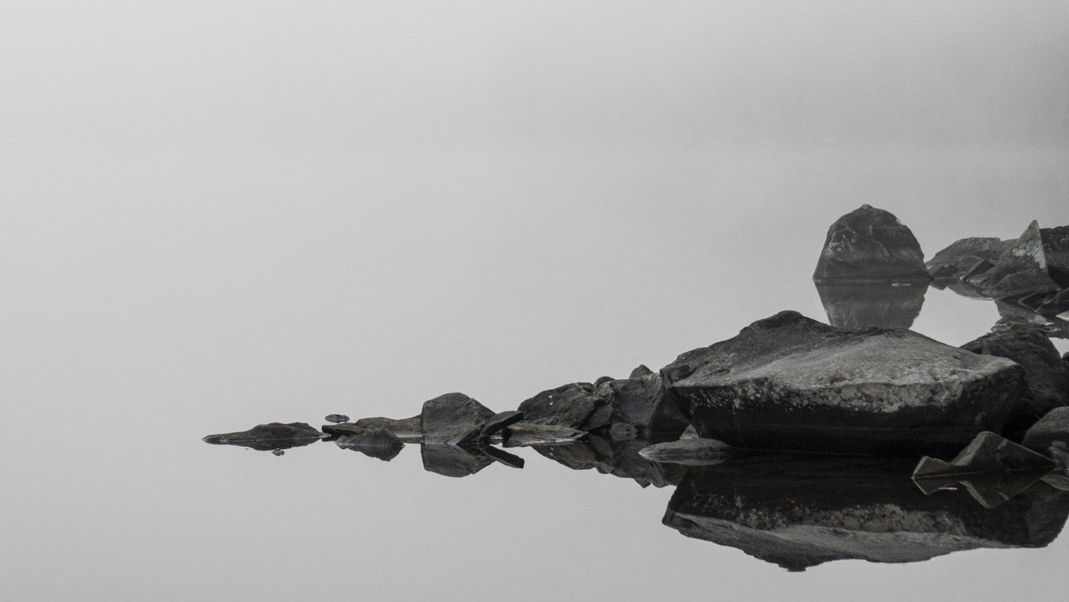 Grey slate reflected in white water, behind all white because of the fog